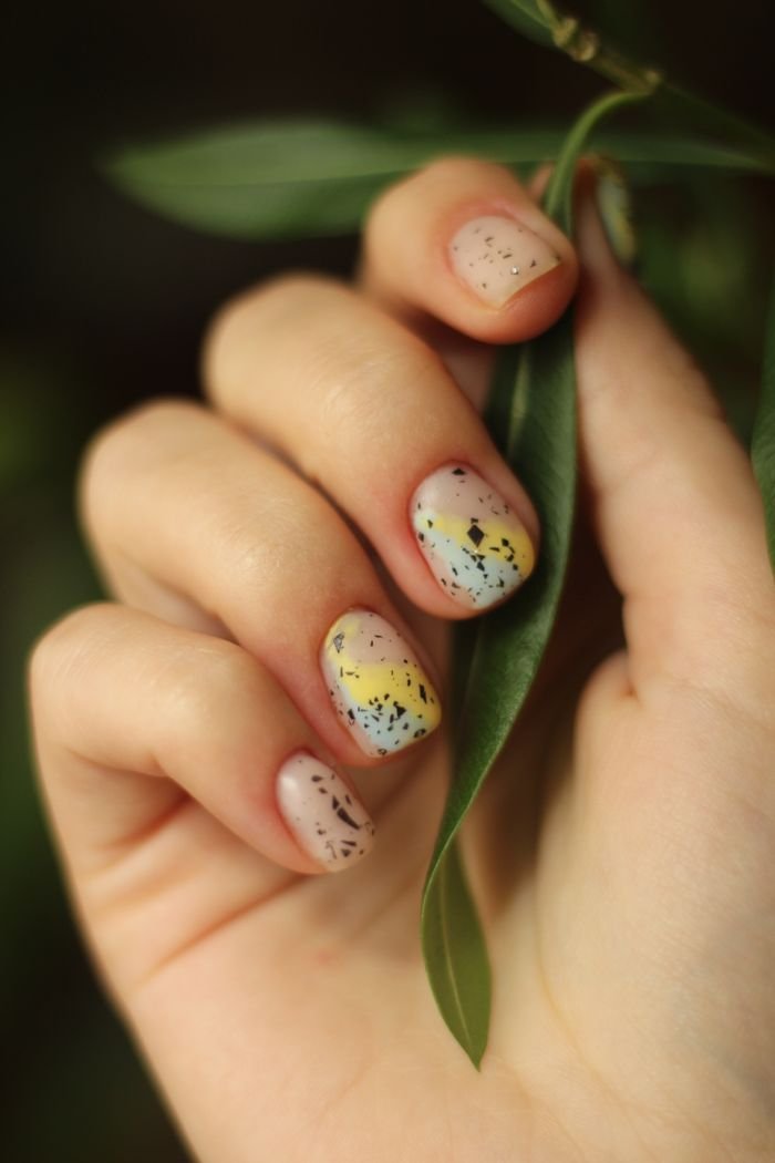 The Art of Drawing Readers In: Your attractive post title goes here Artistic nail design with colorful speckles, surrounded by green leaves for a natural touch.